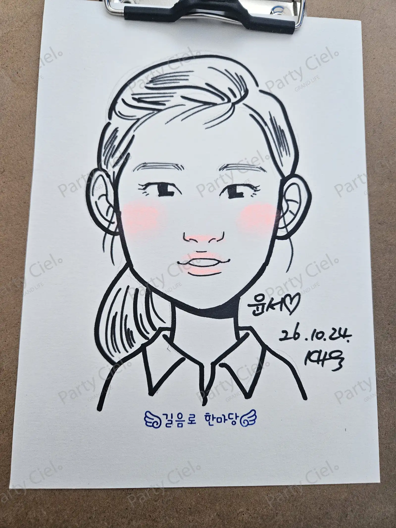 클립보드에 물린 종이에 그린 캐리커처 완성작. 묶은 머리에 깃이 있는 셔츠를 입은 아이를 굵은 검은 선으로 그리고 볼과 코, 입술에 분홍빛을 얹었다
