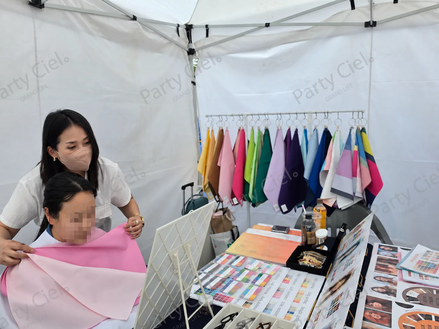천막 부스에서 전문가가 참가자의 얼굴 가까이 분홍 드레이핑 천을 대어 색을 비교하는 모습