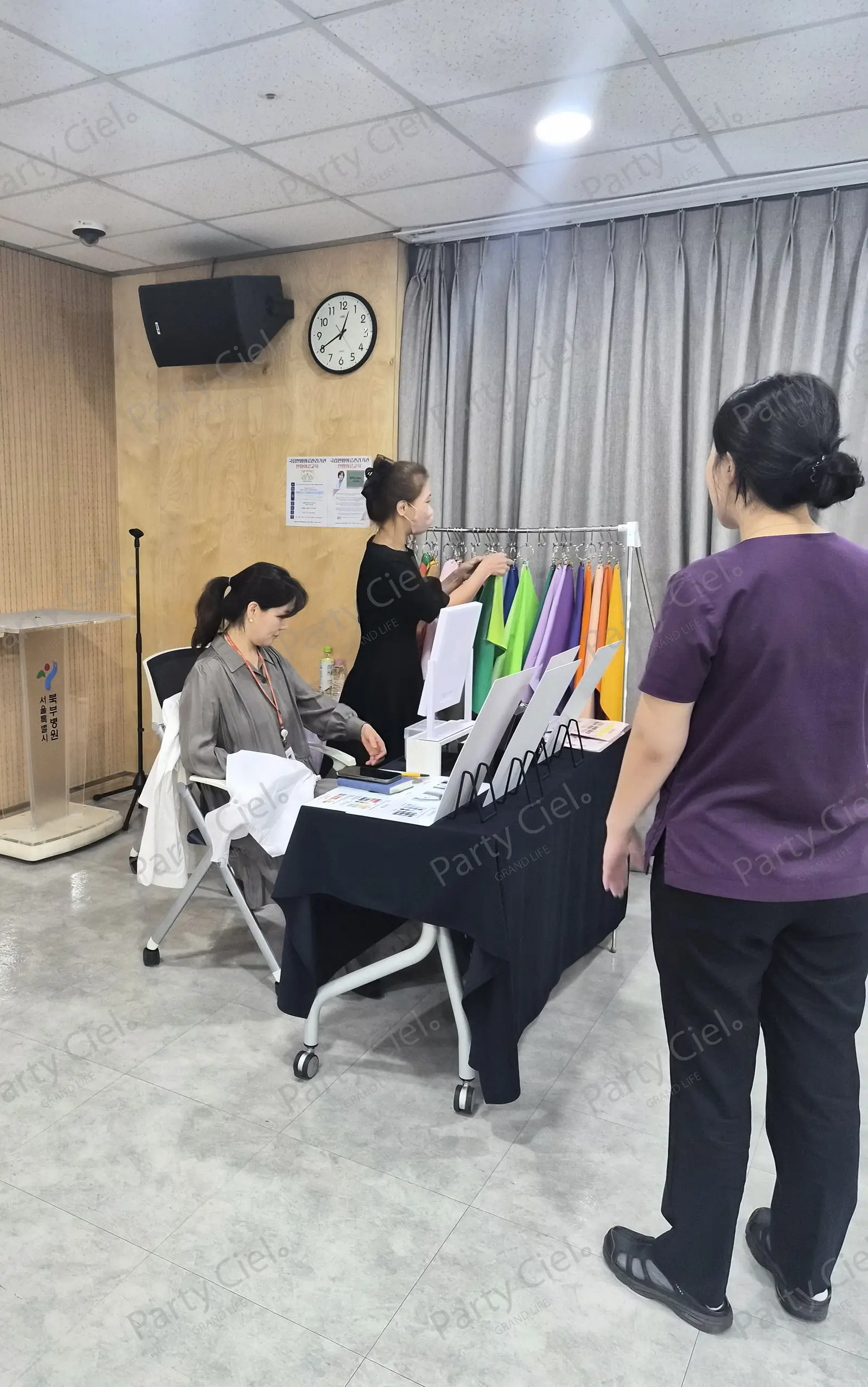홀 안쪽 커튼 앞에 드레이핑 천 행거와 테이블을 둔 퍼스널컬러 부스에서 행거의 천을 정리하는 모습