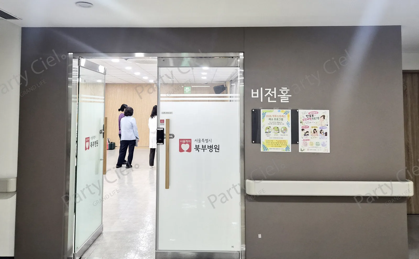 병원 안 실내 홀로 들어가는 행사장 입구의 유리문과 그 너머로 보이는 홀 안쪽