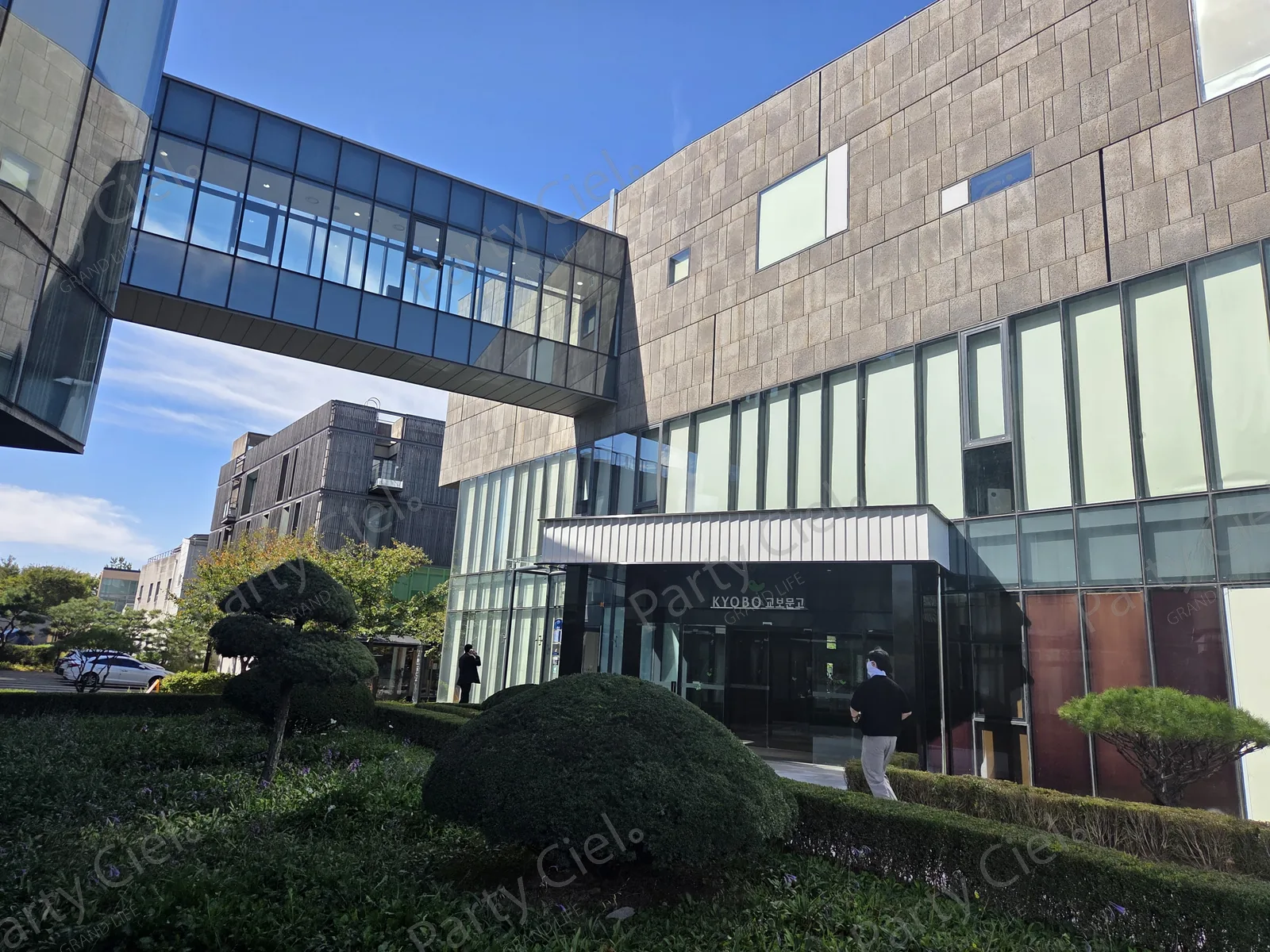 맑은 날 촬영한 교보문고 파주 본사 사옥 외관과 두 건물을 잇는 유리 통로, 앞마당의 정원수