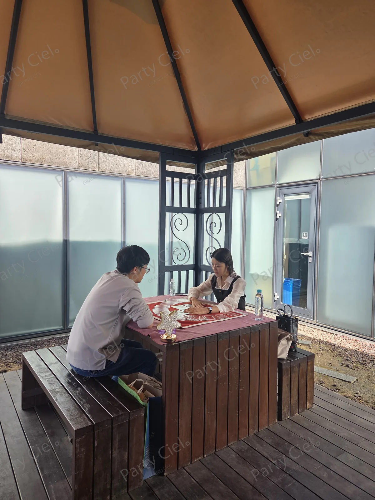 교보문고 파주 본사 테라스 천막 정자 아래 목재 테이블에 붉은 타로 매트를 깔고 타로카드를 부채꼴로 펼쳐 둔 상담 자리