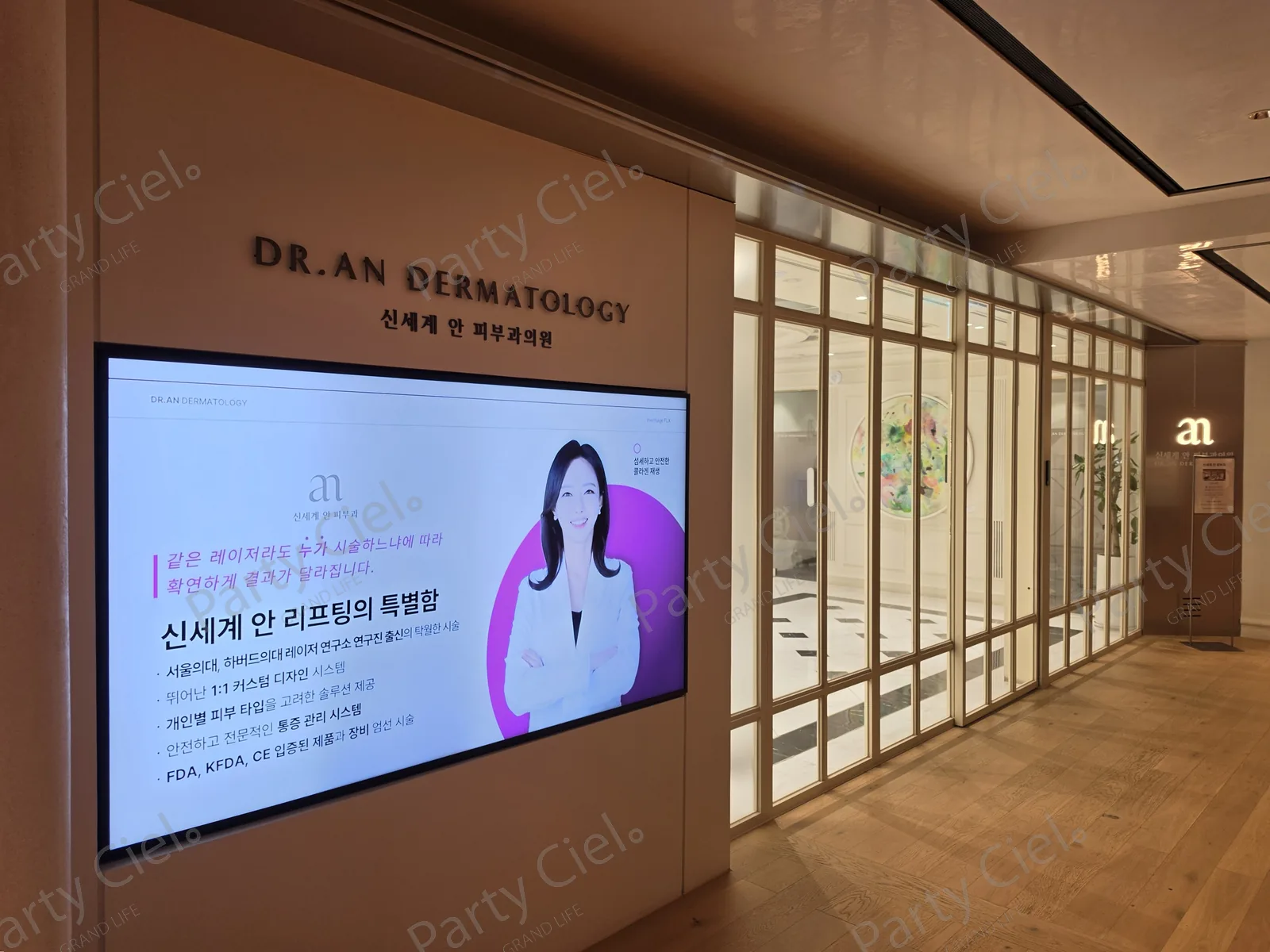 신세계백화점 강남점에 위치한 피부과 의원 입구, 벽면 간판과 안내 화면 옆 유리문 너머로 대기 공간이 보이는 모습