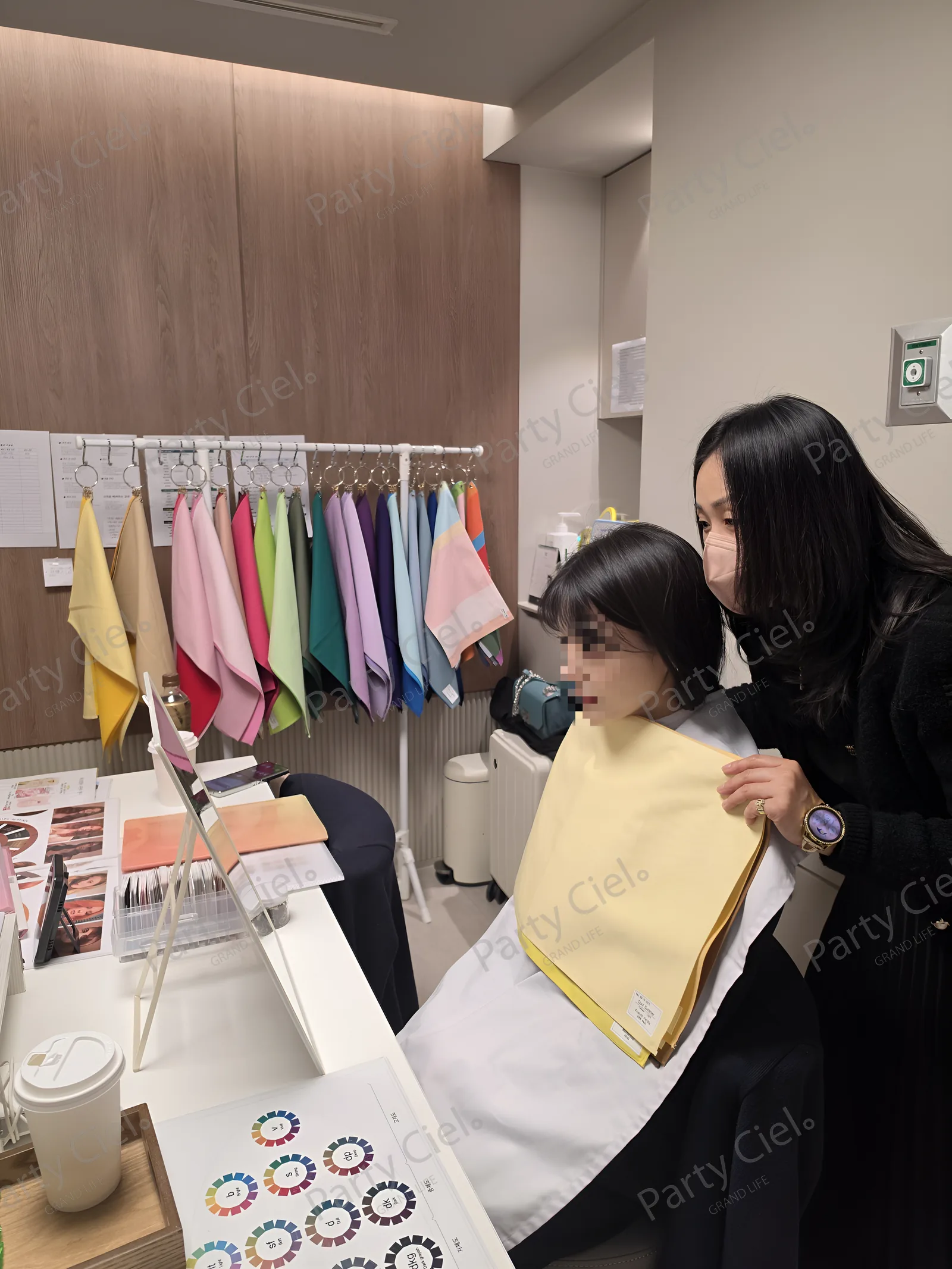 컬러 천 행거 앞에서 퍼스널컬러 전문가가 참여자 어깨에 노란 계열 천을 대어 보며 거울로 피부톤 변화를 함께 확인하는 모습