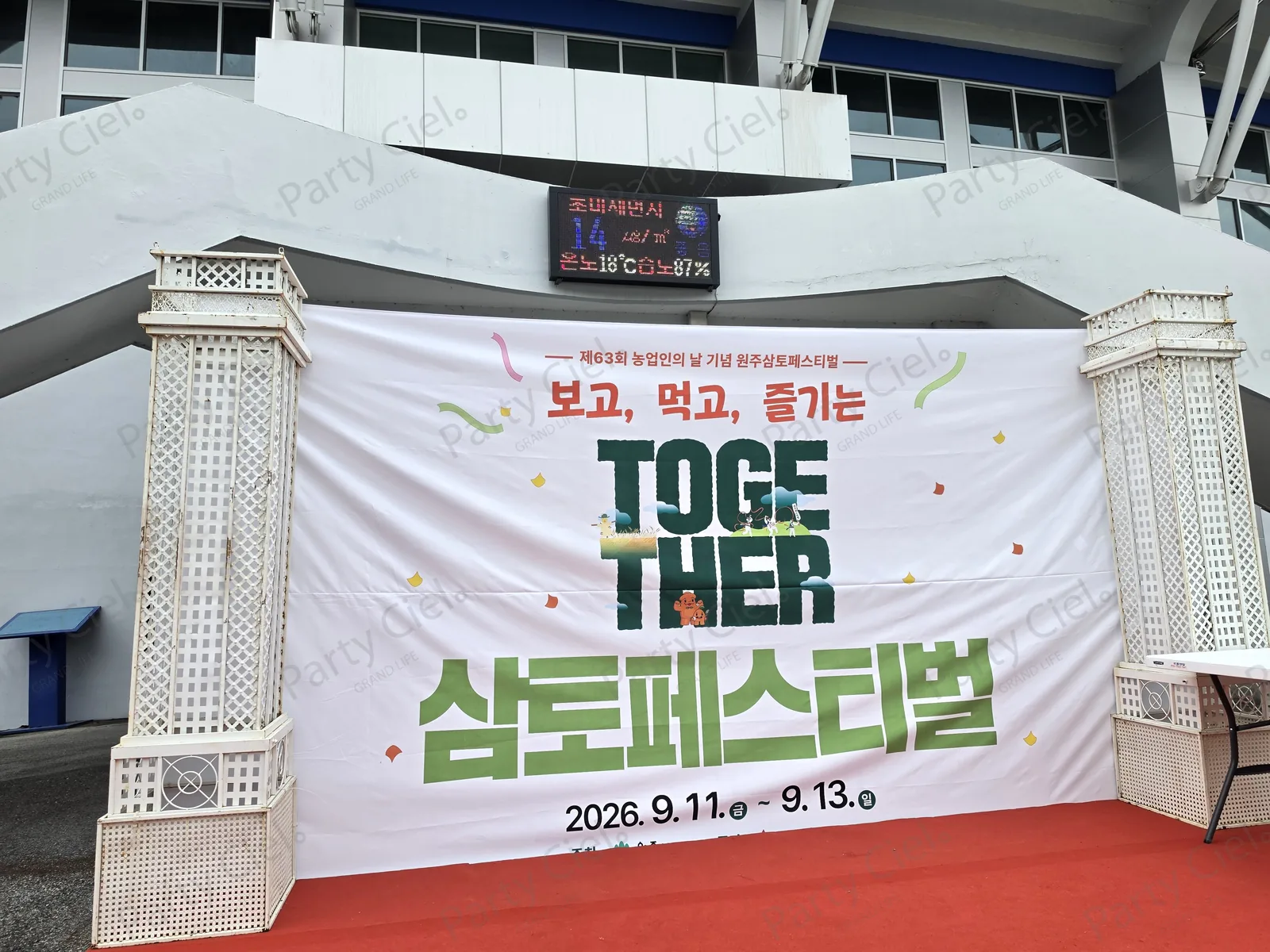 경기장 건물 앞 레드카펫 포토월 현수막 「제63회 농업인의 날 기념 원주삼토페스티벌 · 보고, 먹고, 즐기는 · TOGETHER · 삼토페스티벌 · 2026. 9. 11.(금) - 9. 13.(일)」