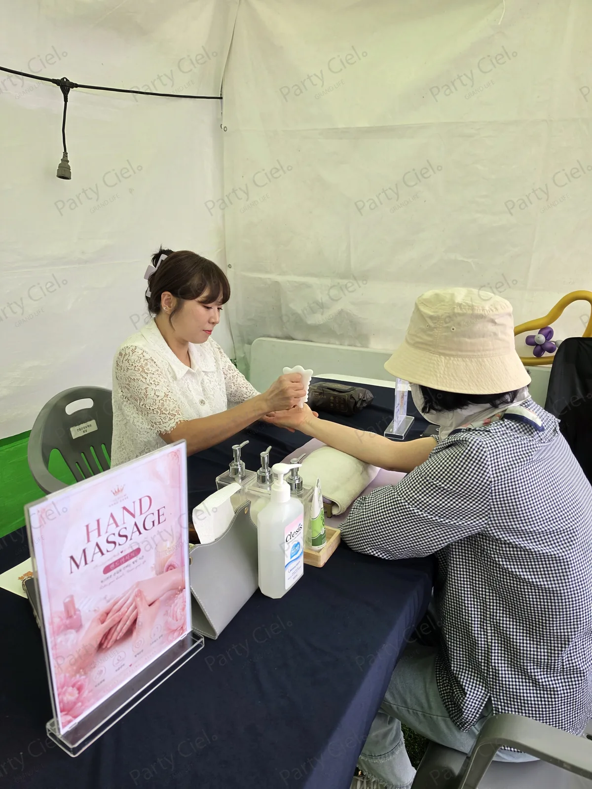 원주삼토페스티벌 파티시엘 핸드마사지 테이블과 HAND MASSAGE 안내판, 마스터가 참가자의 손을 맡아 진행하는 모습