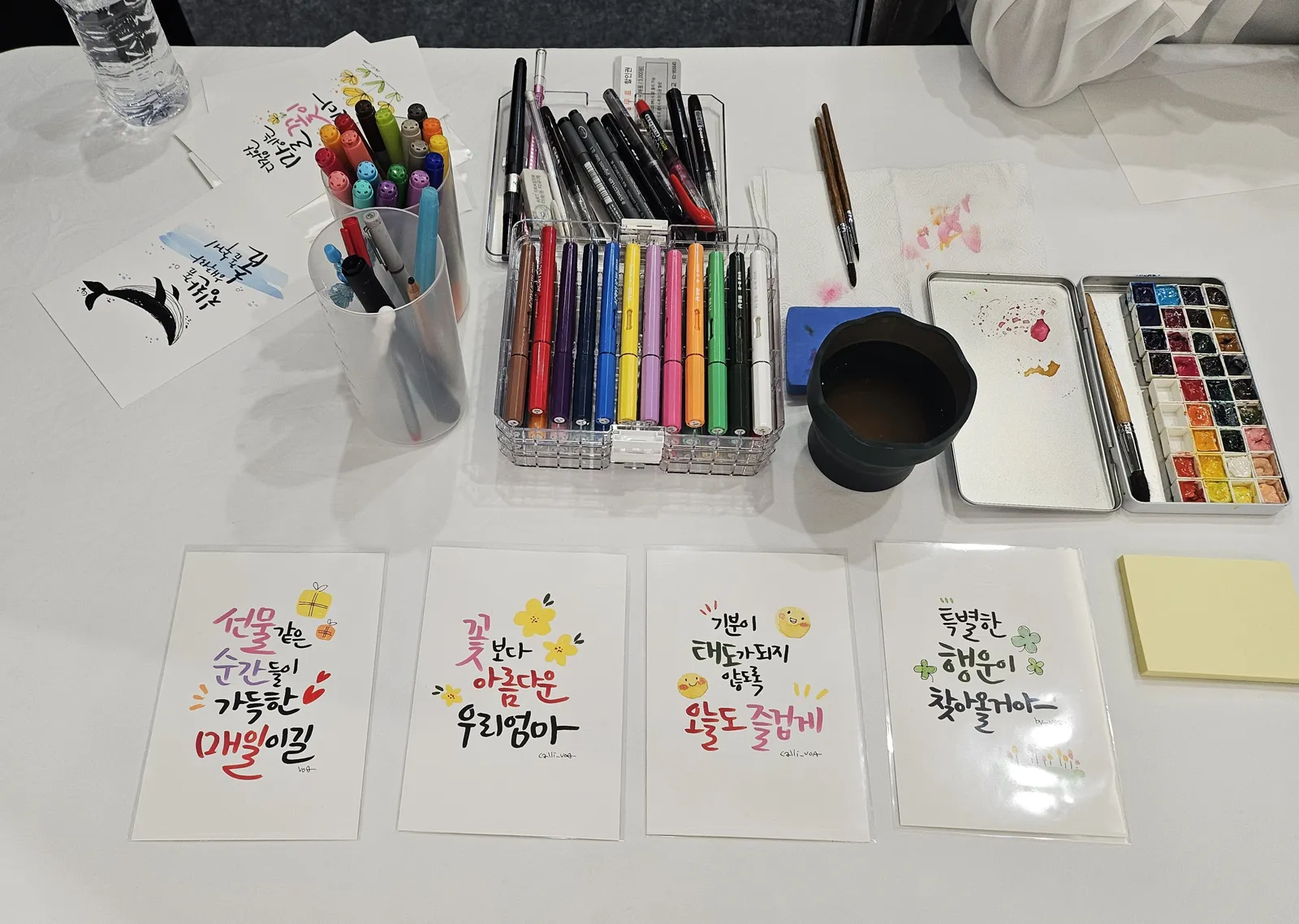캘리그라피 체험부스 마커·수채 물감 도구와 샘플 작품 세팅