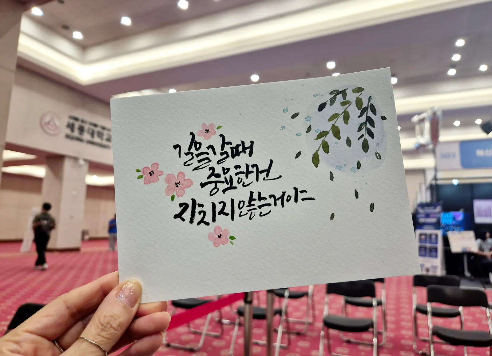 분홍 꽃과 초록 잎 그림을 곁들인 캘리그라피 작품 카드 — 행사장 현장 제작